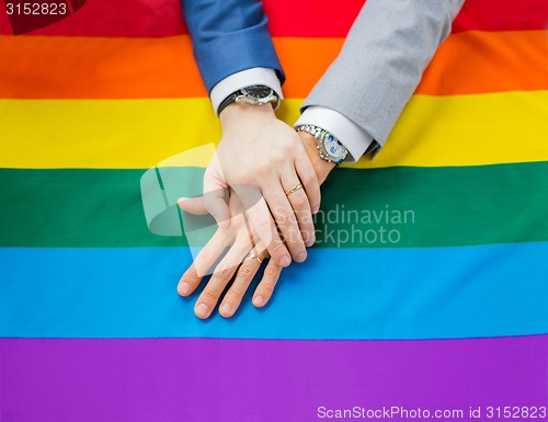 Image of close up of male gay couple hands on rainbow flag