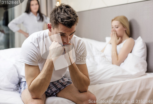 Image of man sitting on the bed with two women on the back