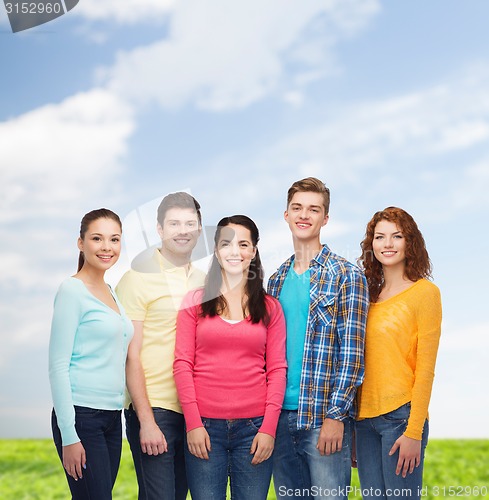 Image of group of smiling teenagers over blue sky and grass