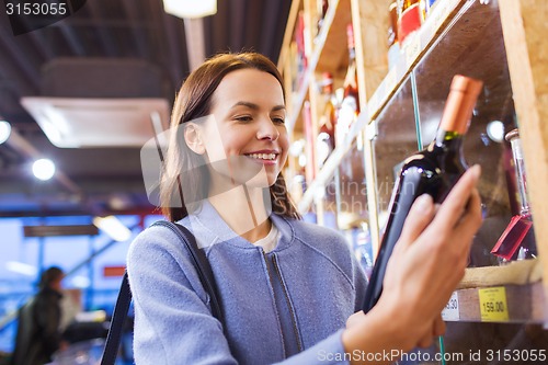 Image of happy woman choosing and buying wine in market
