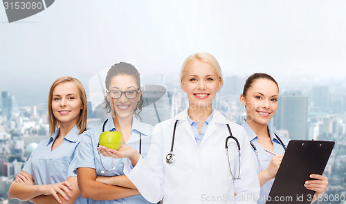 Image of smiling female doctor and nurses with green apple