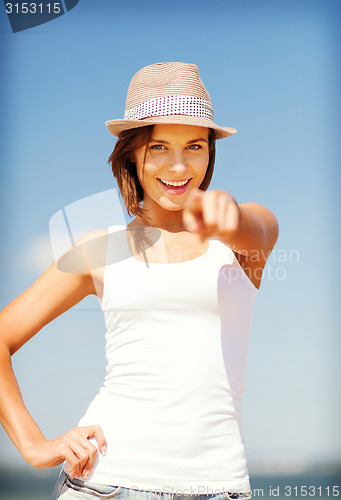 Image of girl in hat pointing at you on the beach
