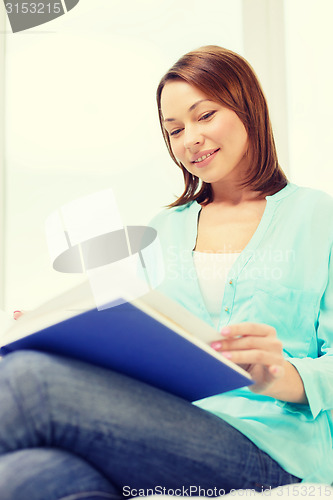 Image of smiling woman reading book and sitting on couch