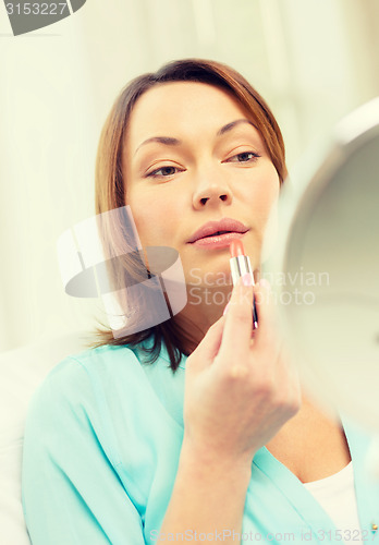 Image of woman applying lipstick and holding mirror