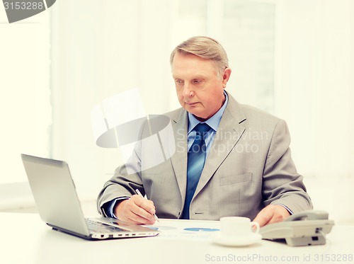 Image of busy older businessman with laptop and telephone