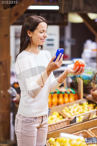 Image of happy woman with smartphone and tomato in market