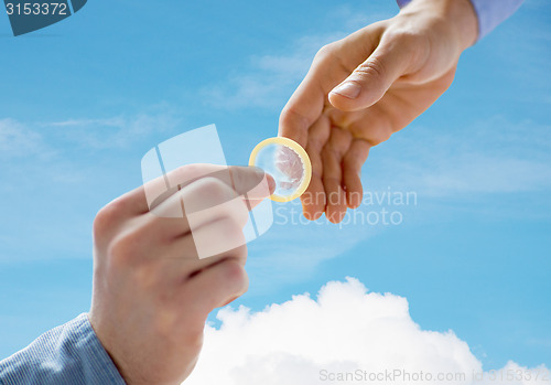 Image of close up of male gay couple hands giving condom