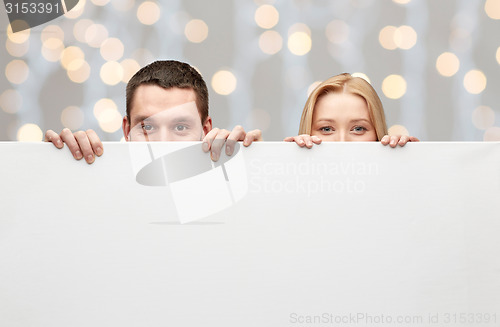 Image of happy couple hiding behind big white blank board