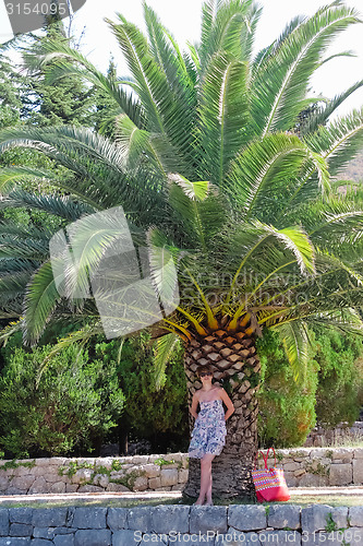 Image of Young woman is standing near palm tree