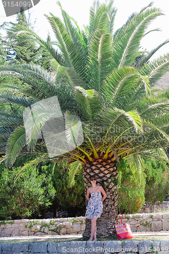 Image of Young woman is standing near palm tree