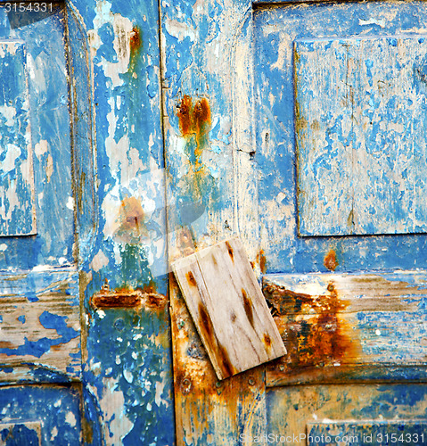 Image of dirty stripped paint in the blue wood door and rusty nail