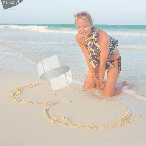 Image of Woman drawing heart on the sand.