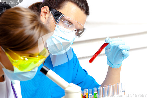 Image of young scientist wearing a mask examines test tube with liquid