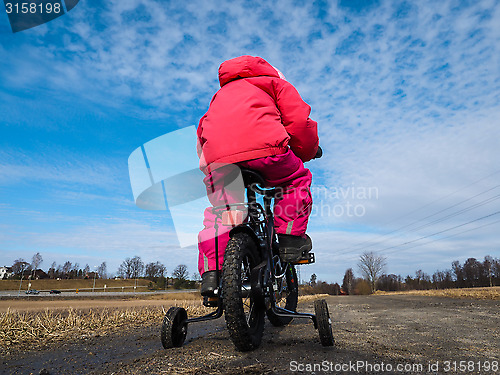 Image of Little girl biker on gravle road with supporting wheels on grave