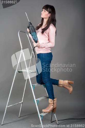 Image of Attractive woman on ladder with heavy drill