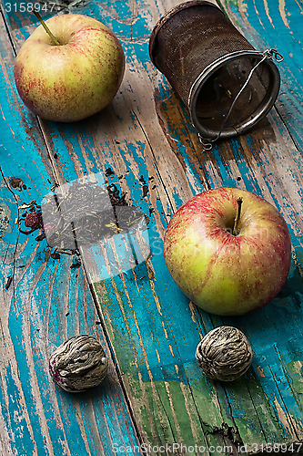 Image of tea leaves and red apple on wooden background