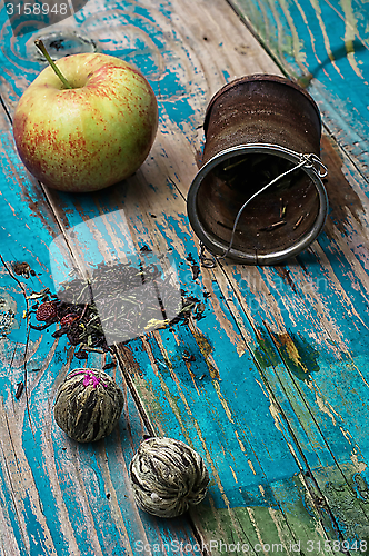Image of tea leaves and red apple on wooden background
