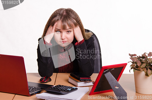 Image of The girl behind the office desk holding head with hands