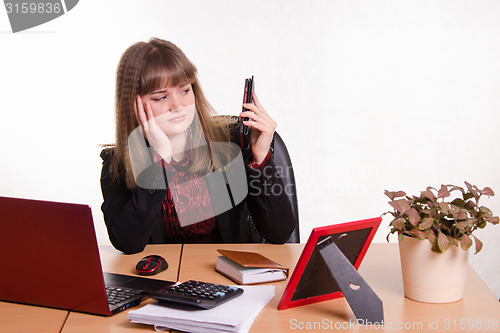 Image of Tired woman sitting office desk, looking at phone