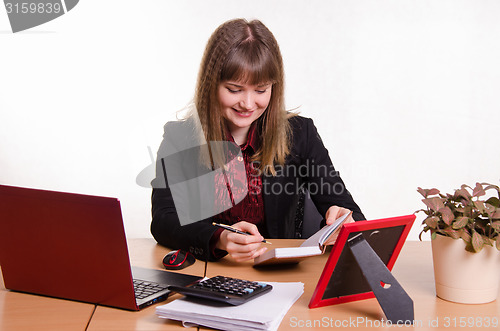Image of Joyful Girl sitting office desk, looking at notebook