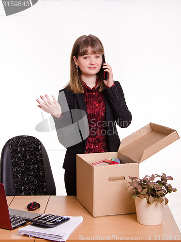 Image of Girl in office collects personal belongings and calling on phone