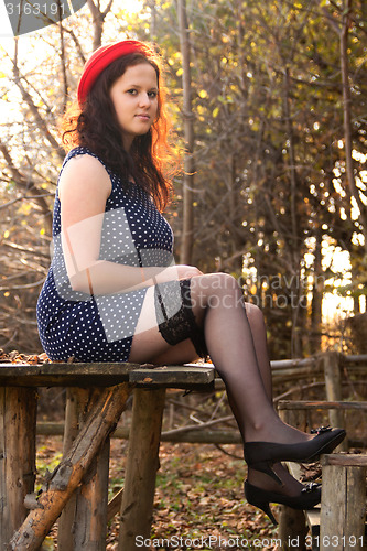 Image of Young woman sitting on a table in a hat