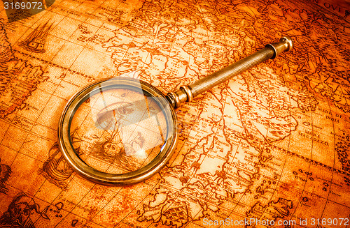 Image of Vintage magnifying glass lies on an ancient world map