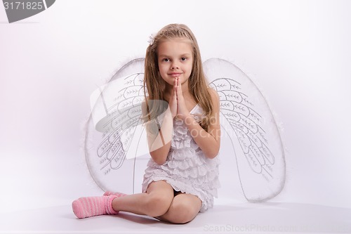 Image of Sitting girl in an angel costume with folded hands