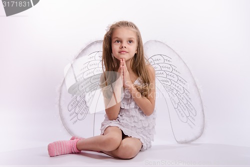 Image of Seated girl with angel wings folded hands