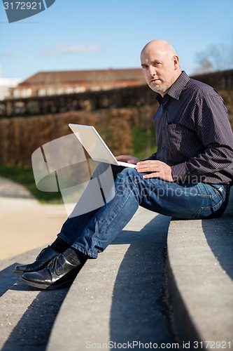 Image of Man sitting on a bench using a laptop