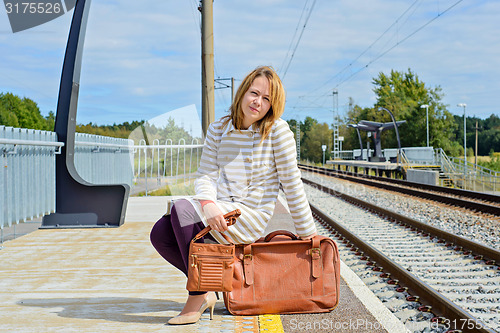 Image of Woman sitting with brown bag and suitcase 