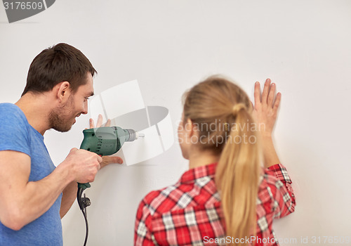 Image of happy couple with drill perforating wall at home