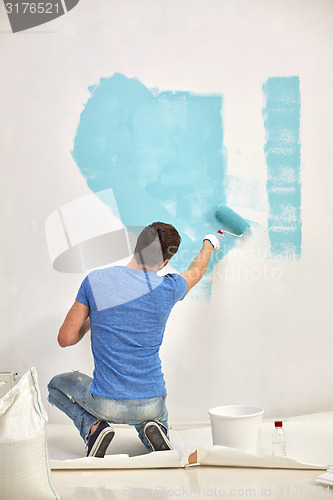 Image of man with roller painting wall in blue at home