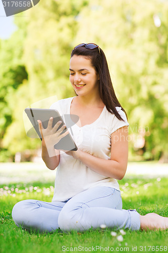 Image of smiling young girl with tablet pc sitting on grass