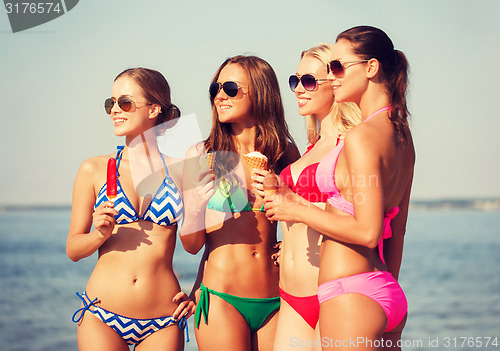 Image of group of smiling women eating ice cream on beach