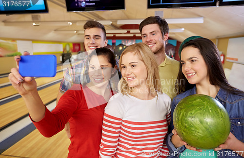 Image of happy friends with smartphone in bowling club