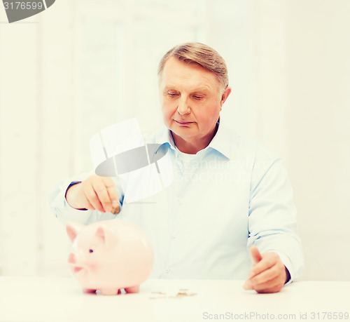 Image of old man putting coin into big piggy bank