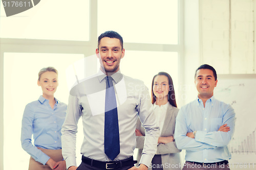 Image of smiling businessman in office with team on back