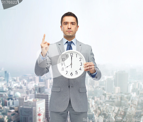 Image of businessman in suit holding clock with 8 o\'clock