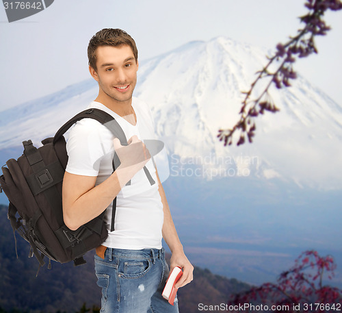 Image of happy young man with backpack and book travelling