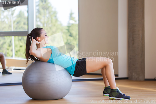 Image of smiling woman with fit ball flexing muscles in gym