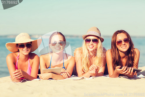 Image of group of smiling young women with tablets on beach