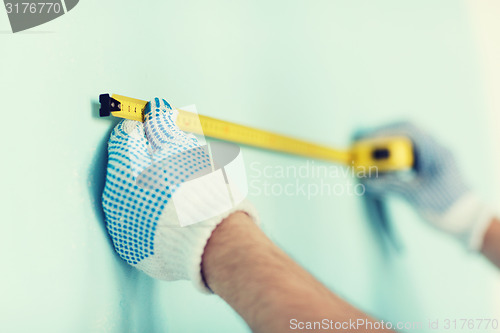 Image of closeup of male in gloves measuring wall with tape