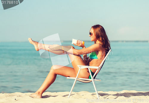 Image of smiling young woman sunbathing in lounge on beach
