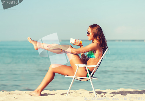 Image of smiling young woman sunbathing in lounge on beach