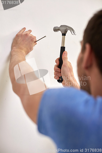 Image of close up of man with hammer hammering nail in wall