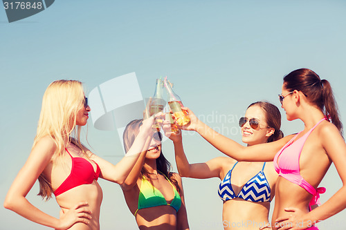 Image of group of smiling young women drinking on beach