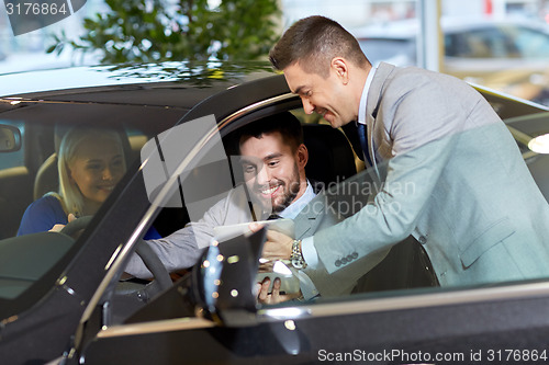 Image of happy couple with car dealer in auto show or salon