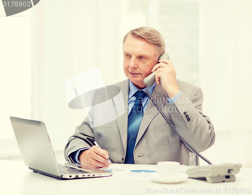 Image of busy older businessman with laptop and telephone
