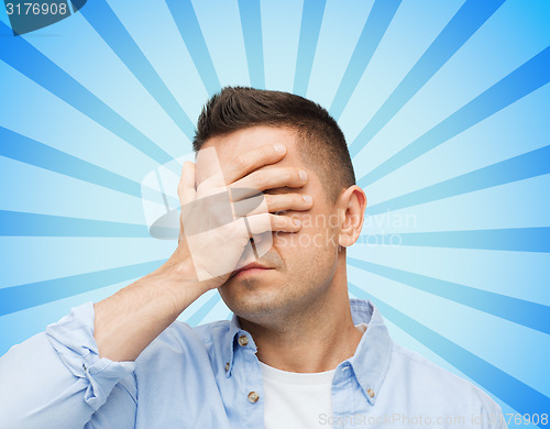 Image of unhappy man covering his eyes by hand